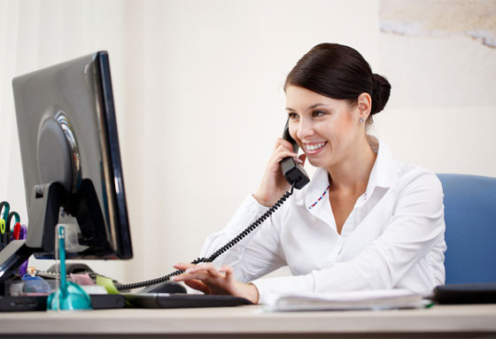 Young woman sitting at a desk in front of a computer talking on the phone